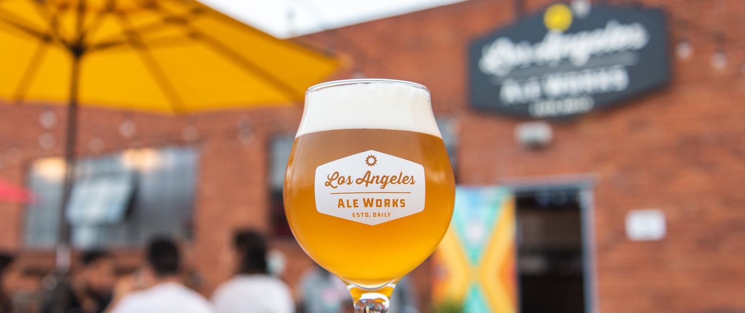 Photo of beer in LA Ale Works branded glass and beer garden out of focus in background