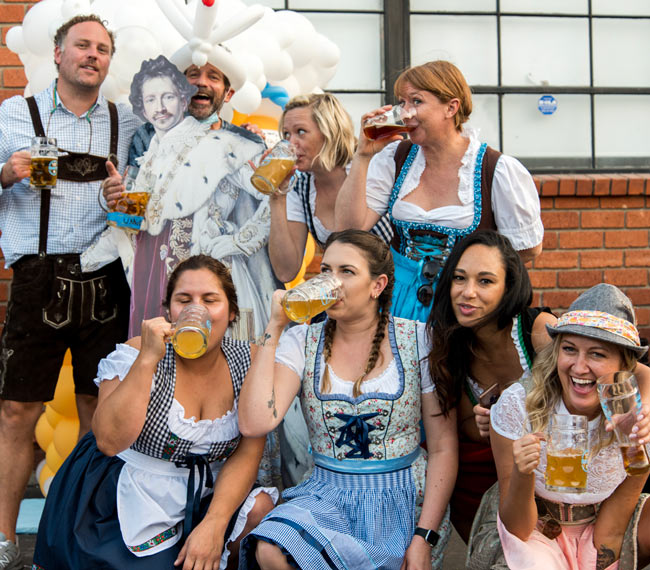 Group of people dressed up in Oktoberfest gear drinking mugs of beer